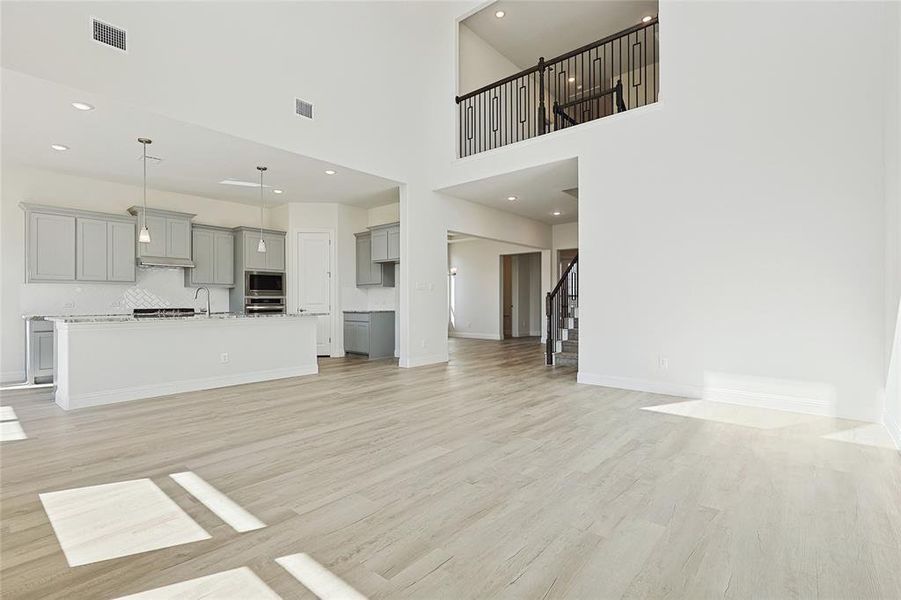 Unfurnished living room featuring a towering ceiling, sink, and light wood-type flooring