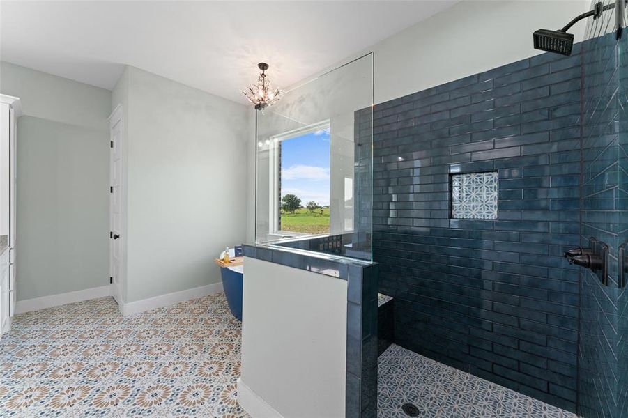 Spacious bathroom featuring patterned floor tiling, a walk-in shower with dark blue subway tile, a built-in shower niche, and a freestanding soaking tub