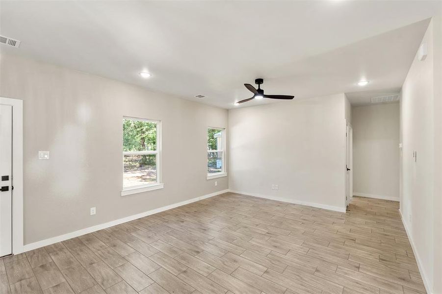 Spacious room featuring wood-look tile flooring, two windows with white trim, a matte black ceiling fan, and recessed lighting Spacious room featuring wood-look tile flooring, two windows with white trim, a matte black ceiling fan, and recessed lighting