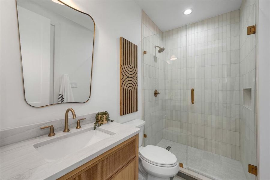 Bathroom featuring a glass-enclosed shower with vertical tile work, a built-in shower niche, and a vanity with a light-toned countertop and an integrated sink