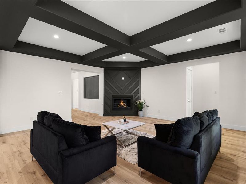 Living area featuring a coffered ceiling with recessed lighting, wood-finish flooring, and a fireplace with a decorative surround