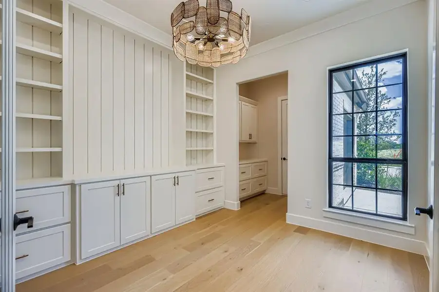 Unfurnished dining area featuring built in shelves, light wood-style flooring, a chandelier, and ornamental molding