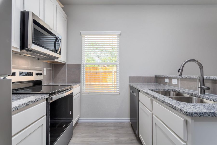 Contemporary kitchen featuring white cabinetry, granite countertops, stainless steel appliances, a tile backsplash, and light wood-finish flooring