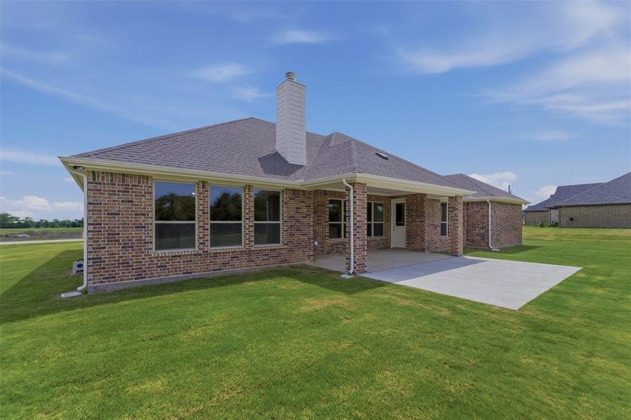 Expansive rear exterior featuring a covered patio, additional concrete pad, large windows, and a brick facade Expansive rear exterior featuring a covered patio, additional concrete pad, large windows, and a brick facade
