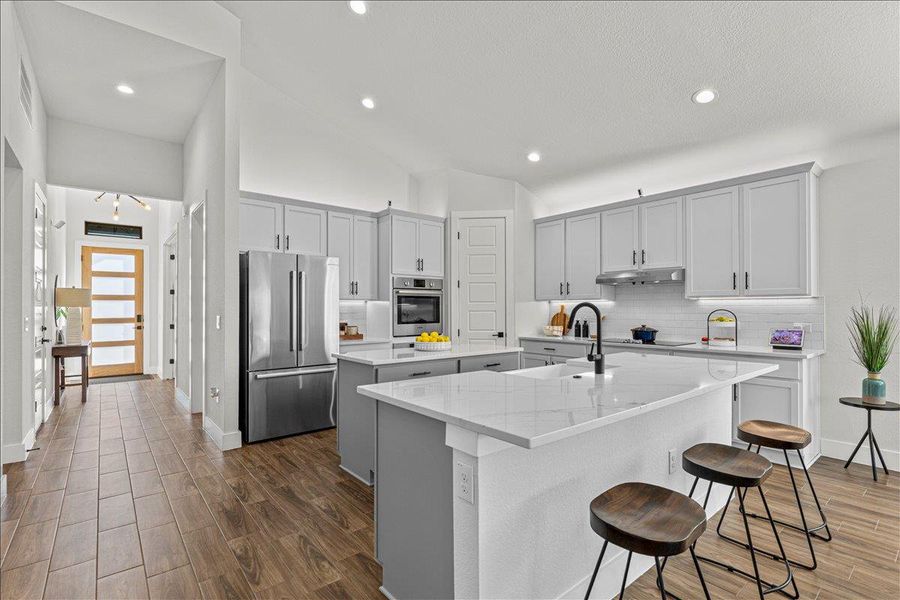 Kitchen featuring dark wood-type flooring, appliances with stainless steel finishes, light stone countertops, recessed lighting, and gray cabinetry
