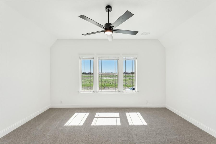 Empty bedroom with vaulted ceiling, ceiling fan, carpet flooring, and triple window with open field view Empty bedroom with vaulted ceiling, ceiling fan, carpet flooring, and triple window with open field view