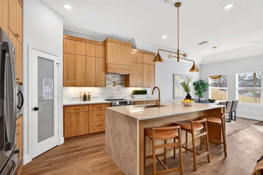 Kitchen featuring a breakfast bar, light stone countertops, tasteful backsplash, pendant lighting, and light wood-style floors