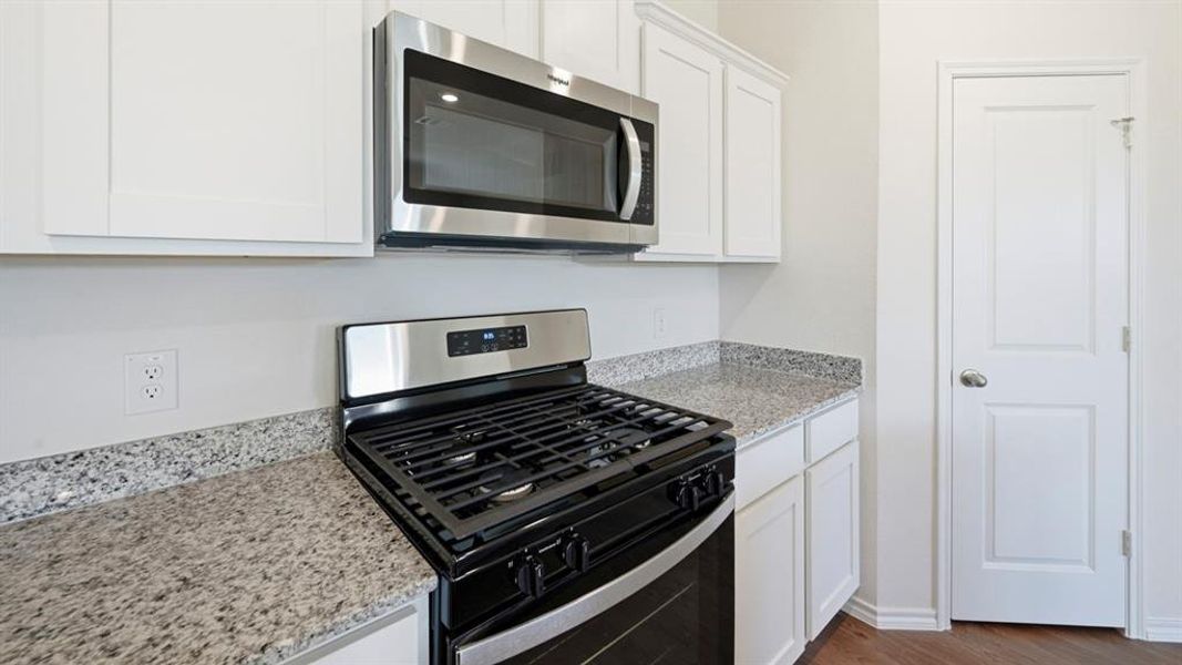 Kitchen featuring appliances with stainless steel finishes, light stone countertops, white cabinets, and dark wood-style flooring