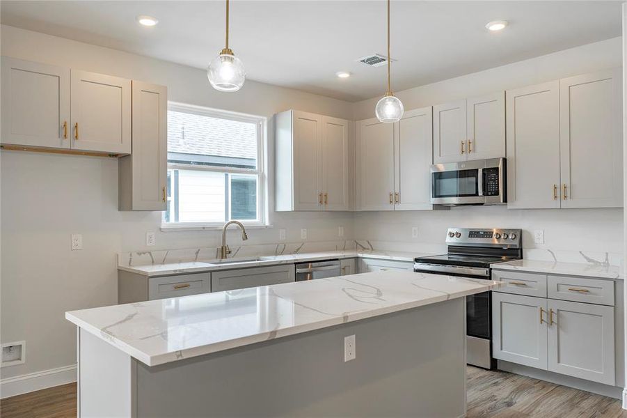 Kitchen featuring appliances with stainless steel finishes, a kitchen island, hanging light fixtures, and light stone countertops