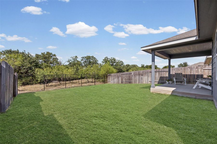 A covered back porch overlooks a grassy yard enclosed by wood and wrought iron fencing.