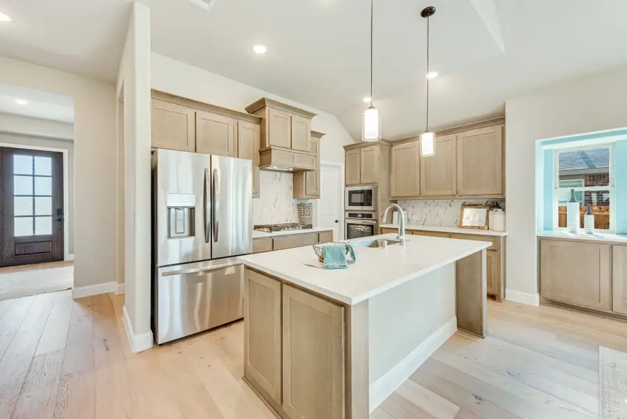 Kitchen with tan wood cabinets, center island with white countertop, stainless steel appliances, and light hardwood floors
