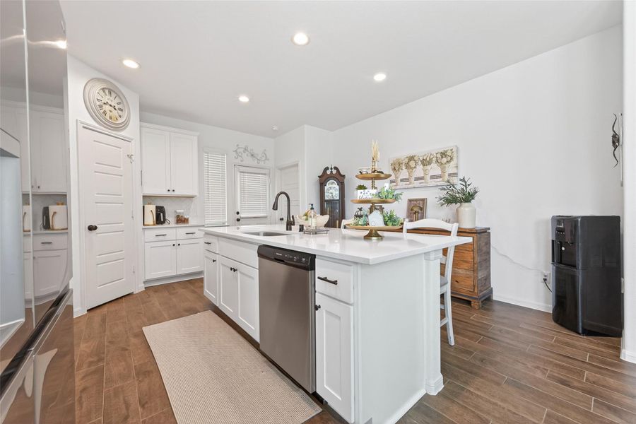 This kitchen features a modern design with white cabinetry, a large island with a sink, walk in pantry and stainless steel appliances. It has a cozy, inviting atmosphere with wood-look tile flooring. This kitchen features a modern design with white cabinetry, a large island with a sink, walk in pantry and stainless steel appliances. It has a cozy, inviting atmosphere with wood-look tile flooring.