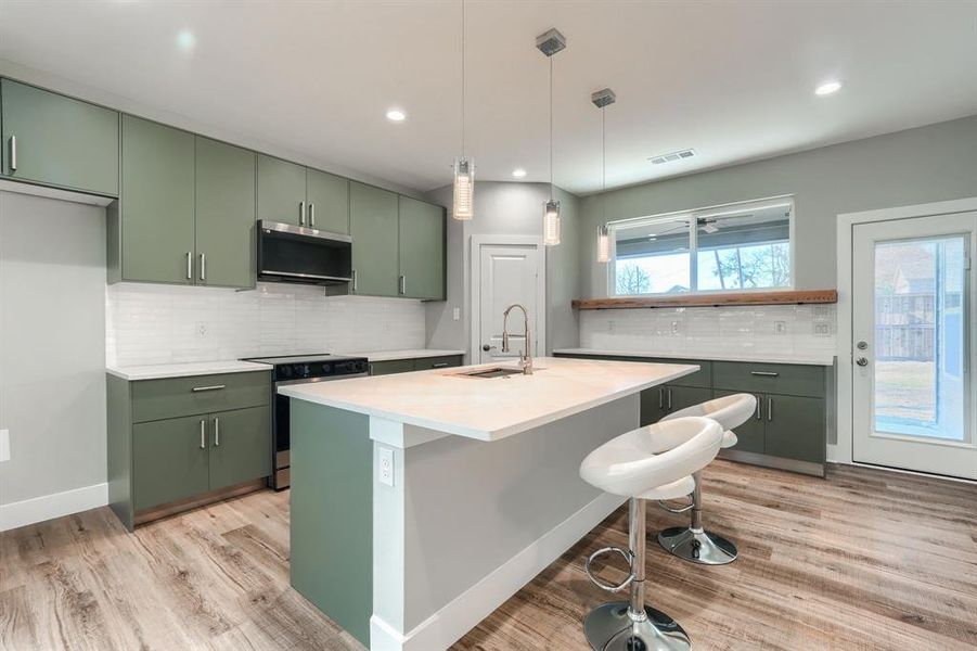 Kitchen with pendant lighting, sink, green cabinetry, appliances with stainless steel finishes, and tasteful backsplash