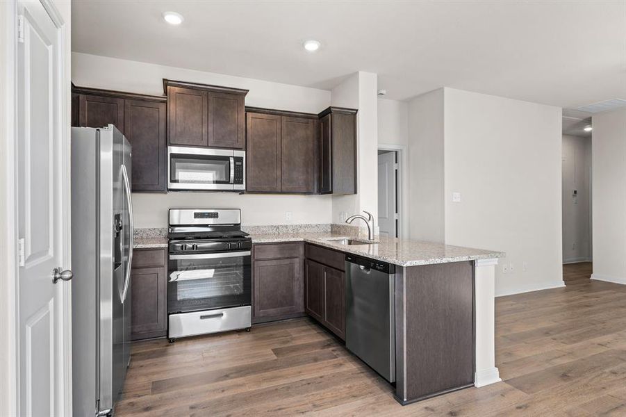 Kitchen featuring appliances with stainless steel finishes, dark brown cabinetry, light stone counters, light wood-type flooring, and recessed lighting