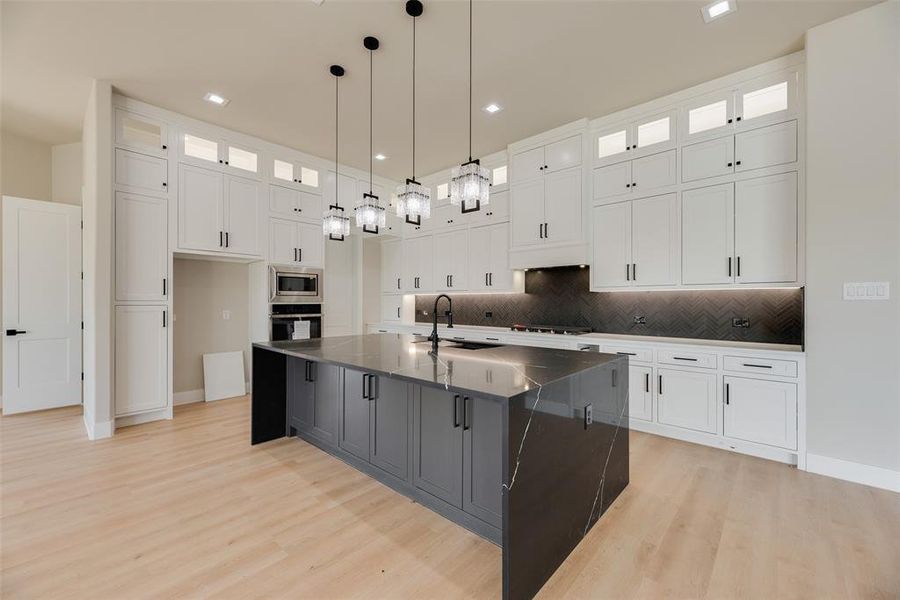 Kitchen with glass insert cabinets, pendant lighting, light wood finished floors, a large island with sink, and dual tone cabinetry