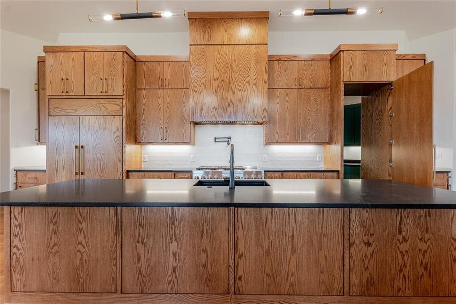 Kitchen featuring decorative backsplash, a spacious island, stainless steel gas cooktop, and dark stone countertops