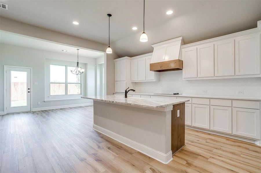 Kitchen featuring white cabinets, custom exhaust hood, tasteful backsplash, and light wood-type flooring