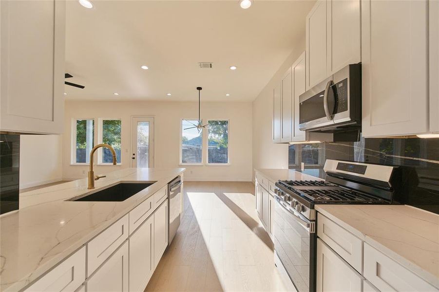 Kitchen featuring light wood-type flooring, light stone counters, sink, hanging light fixtures, and appliances with stainless steel finishes