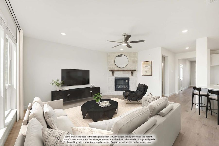 Open living room with stone fireplace, ceiling fan, hardwood floors, and large sectional sofa