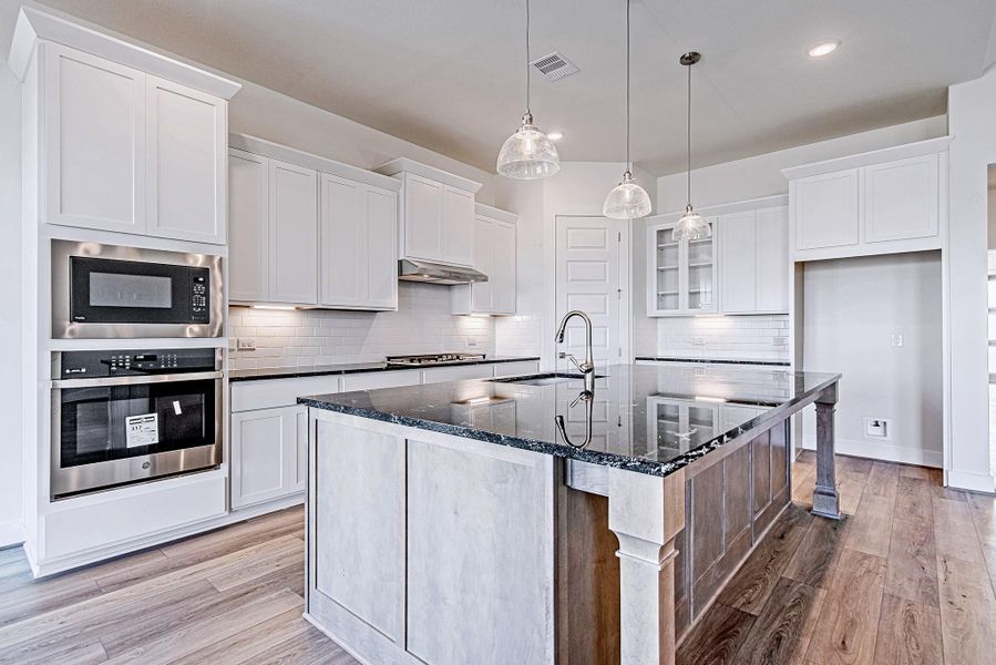 Chef’s kitchen featuring large island, white cabinetry, and built-in appliances.