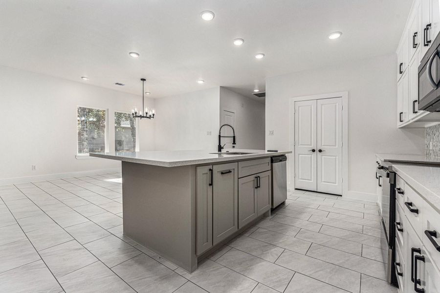 This photo showcases a modern, open-concept kitchen and dining area with a large central island, sleek cabinetry, stainless steel appliances, and ample natural light from two large windows. The space features recessed lighting and a stylish chandelier, enhancing the bright, contemporary feel.