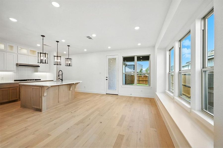 Kitchen featuring a breakfast bar area, light wood-style flooring, glass insert cabinets, pendant lighting, and a center island with sink Kitchen featuring a breakfast bar area, light wood-style flooring, glass insert cabinets, pendant lighting, and a center island with sink