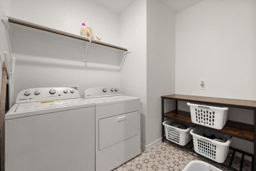Utility room featuring patterned floor tiles, a built-in shelf with hanging rod, and a freestanding shelving unit with wood-finish tops