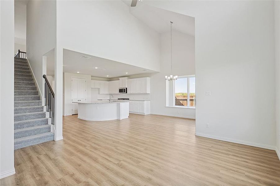 Unfurnished living room featuring a high ceiling, ceiling fan with notable chandelier, and light hardwood / wood-style floors