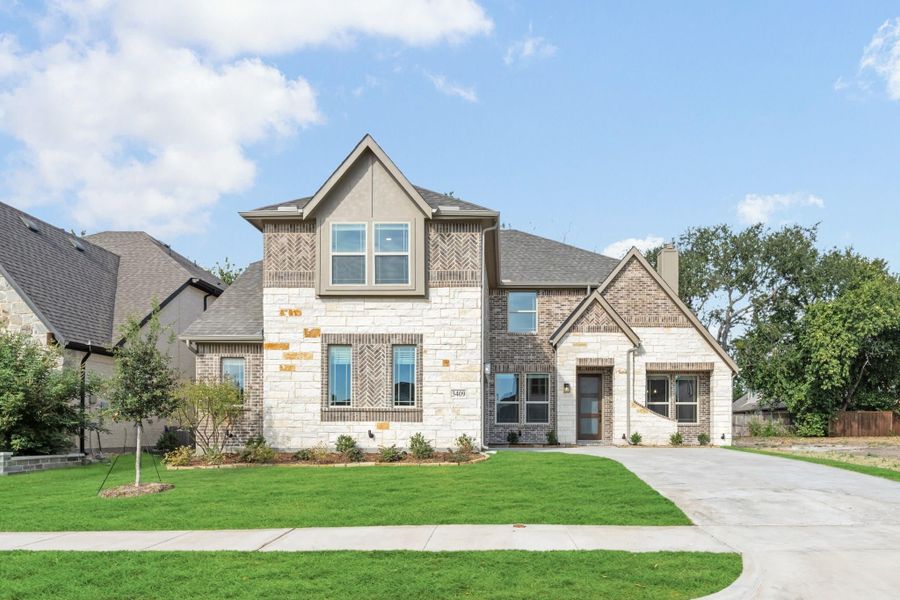 Two-story home with stone and brick exterior, pitched roof, and concrete driveway with green front lawn