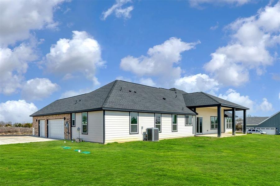 Back of house featuring central air condition unit, a lawn, driveway, and a garage