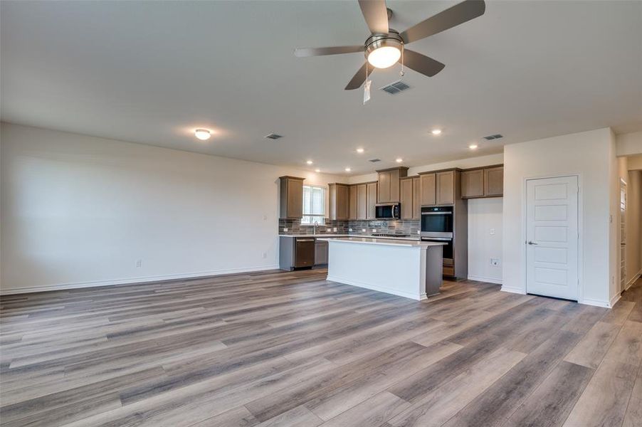 Kitchen featuring open floor plan, light wood-type flooring, a ceiling fan, light countertops, and a kitchen island Kitchen featuring open floor plan, light wood-type flooring, a ceiling fan, light countertops, and a kitchen island