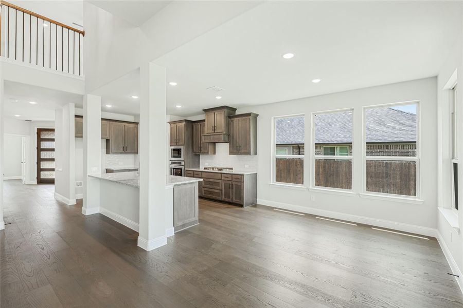Open-concept living area and kitchen with dark wood cabinets, center island, hardwood floors, and two-story ceiling. Open-concept living area and kitchen with dark wood cabinets, center island, hardwood floors, and two-story ceiling.