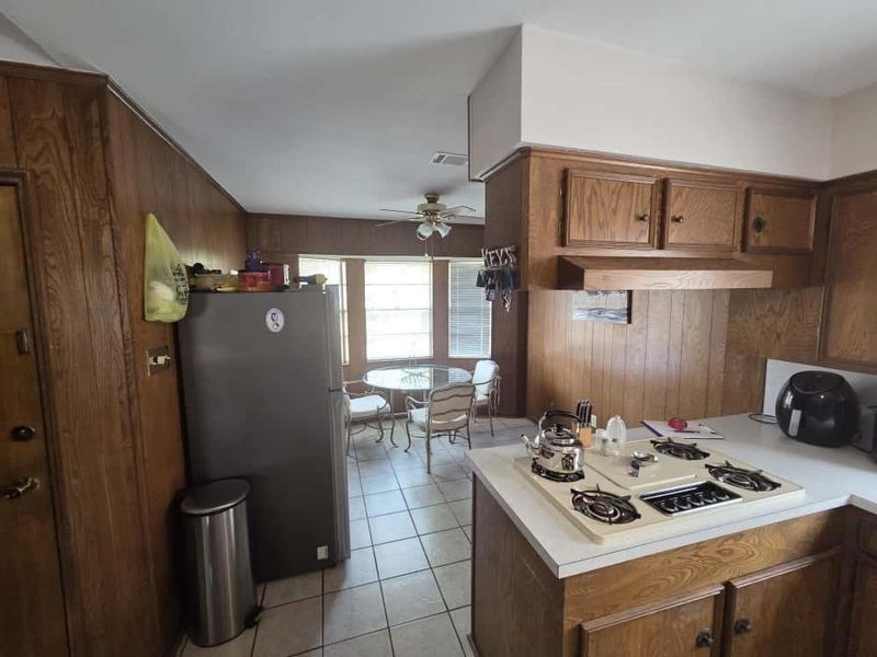 Kitchen with wood walls, freestanding refrigerator, light countertops, brown cabinets, and light tile patterned flooring Kitchen with wood walls, freestanding refrigerator, light countertops, brown cabinets, and light tile patterned flooring