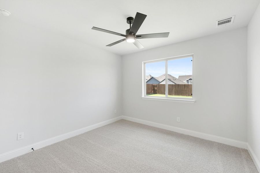 Empty bedroom with light carpet, white walls, ceiling fan, and single window with backyard view Empty bedroom with light carpet, white walls, ceiling fan, and single window with backyard view