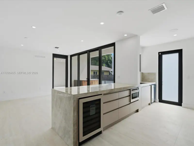 Kitchen featuring an expansive stone-topped island with an integrated wine refrigerator, custom flat-panel cabinetry, recessed lighting, and expansive glass sliding doors Kitchen featuring an expansive stone-topped island with an integrated wine refrigerator, custom flat-panel cabinetry, recessed lighting, and expansive glass sliding doors