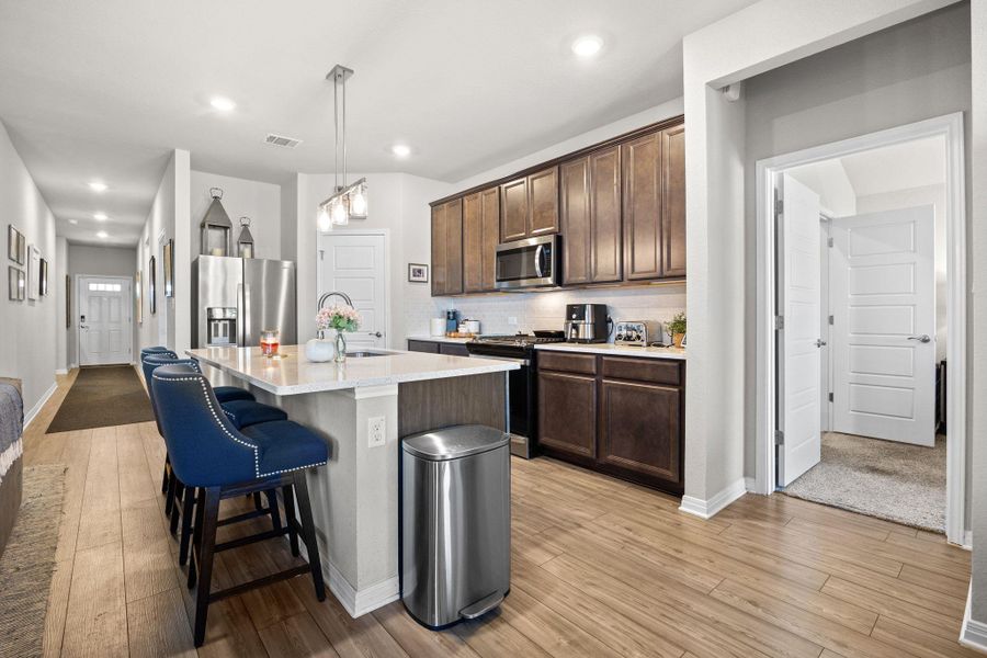 Kitchen featuring decorative backsplash, a kitchen bar, appliances with stainless steel finishes, dark brown cabinetry, and light wood-style flooring Kitchen featuring decorative backsplash, a kitchen bar, appliances with stainless steel finishes, dark brown cabinetry, and light wood-style flooring