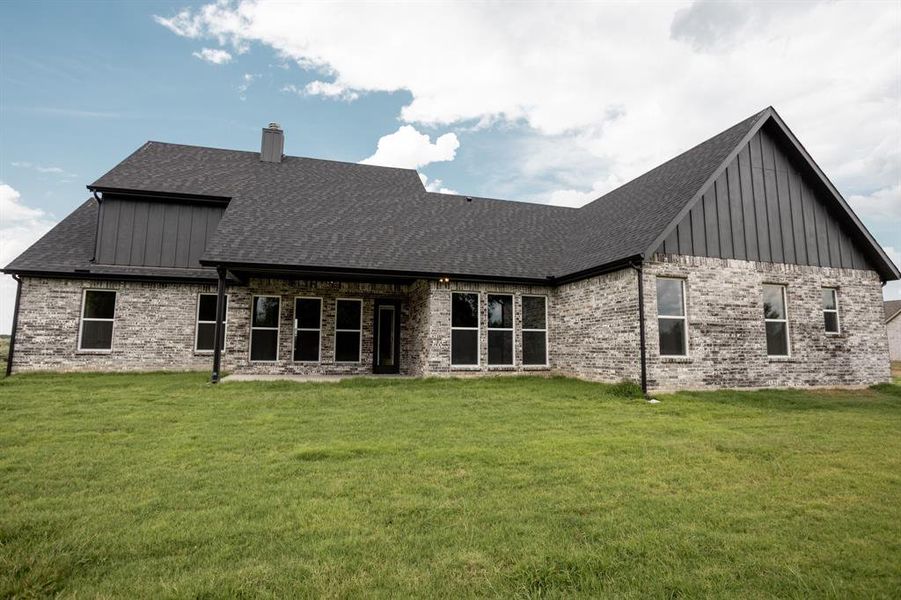 Rear view of property featuring board and batten siding, a patio, a lawn, brick siding, and a chimney Rear view of property featuring board and batten siding, a patio, a lawn, brick siding, and a chimney