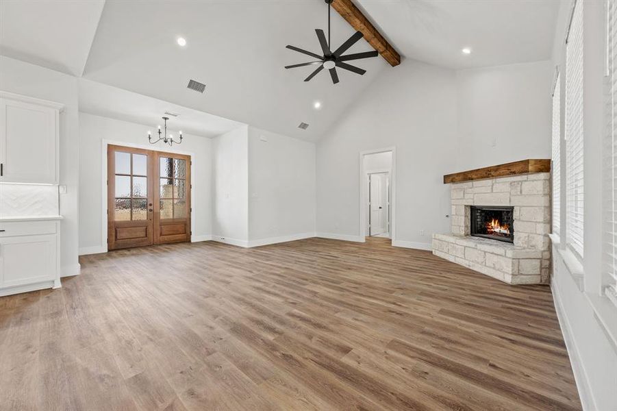 Unfurnished living room featuring beam ceiling, a stone fireplace, a ceiling fan, light wood-style flooring, and high vaulted ceiling Unfurnished living room featuring beam ceiling, a stone fireplace, a ceiling fan, light wood-style flooring, and high vaulted ceiling