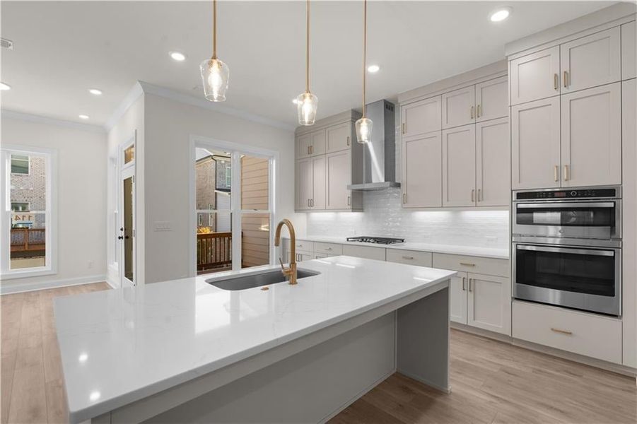 Kitchen featuring light wood finished floors, ornamental molding, tasteful backsplash, gray cabinets, and decorative light fixtures