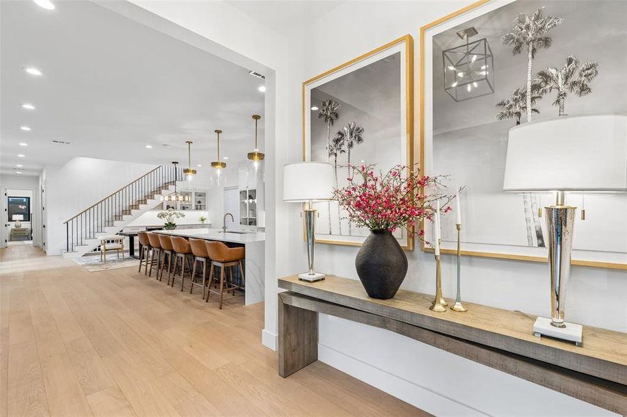 Welcoming entry with designer finishes and warm wood floors, opening to a bright, open-concept living and kitchen area.