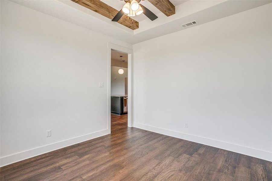 Spare room featuring dark wood-type flooring, beamed ceiling, and ceiling fan