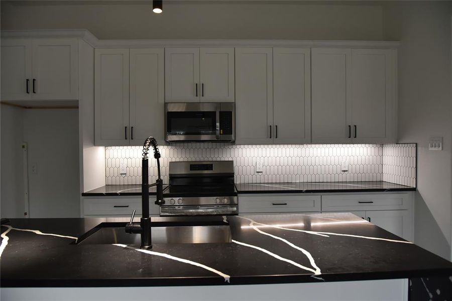 Kitchen featuring decorative backsplash, stainless steel appliances, white cabinetry, and sink