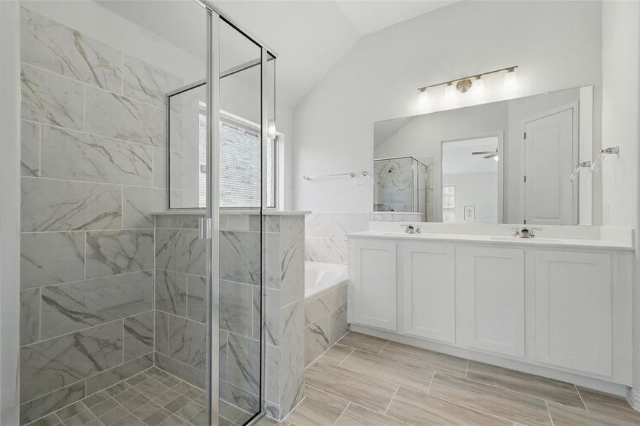 Full bath featuring double vanity, a stall shower, a bath, vaulted ceiling, and a sink