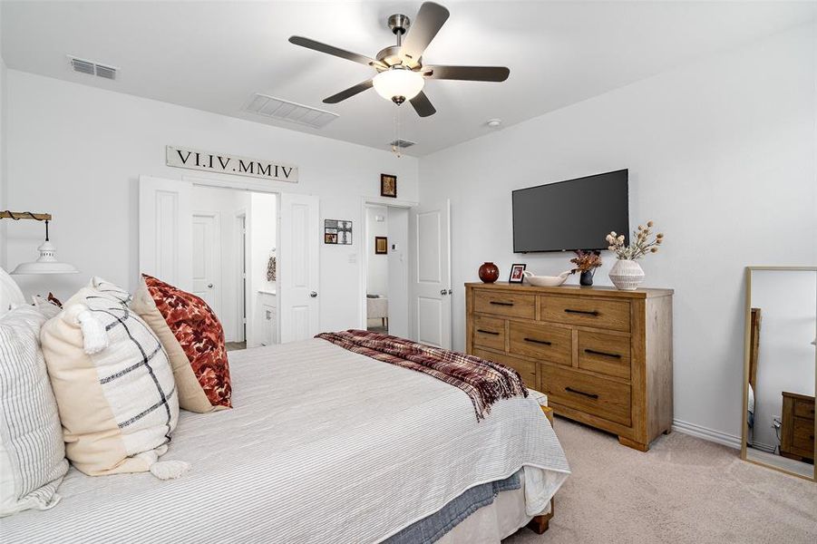 The bedroom features light-colored carpeting, a ceiling fan, and white walls