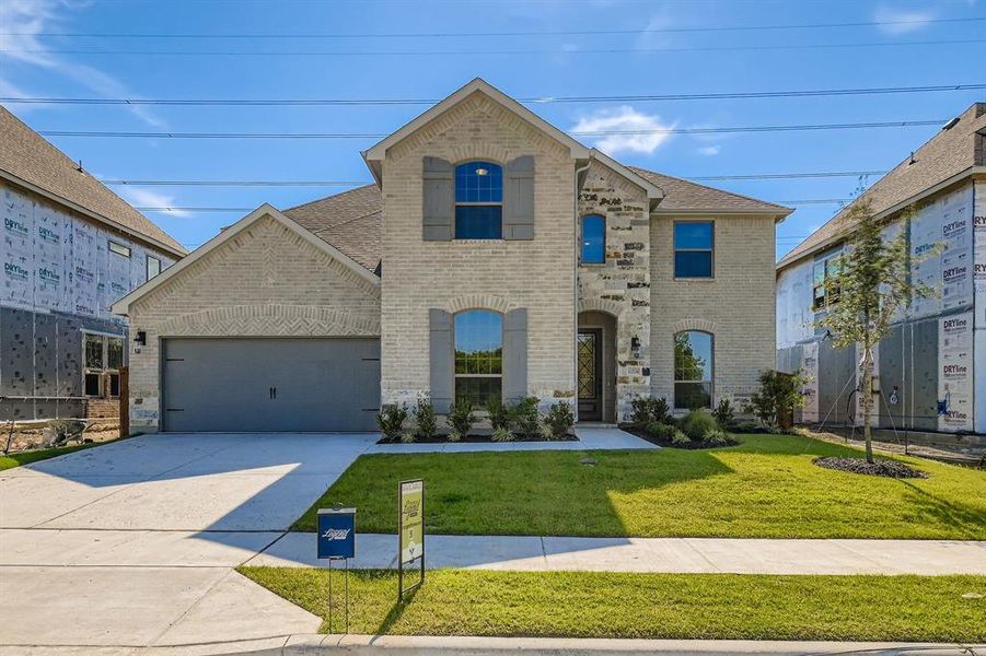 French provincial home featuring brick siding, a garage, concrete driveway, and a front yard