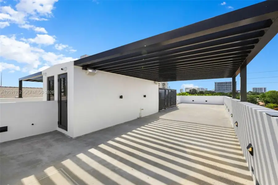 Rooftop terrace featuring a flat concrete surface, a black metal pergola, wall-mounted exterior lighting, and solid perimeter walls Rooftop terrace featuring a flat concrete surface, a black metal pergola, wall-mounted exterior lighting, and solid perimeter walls