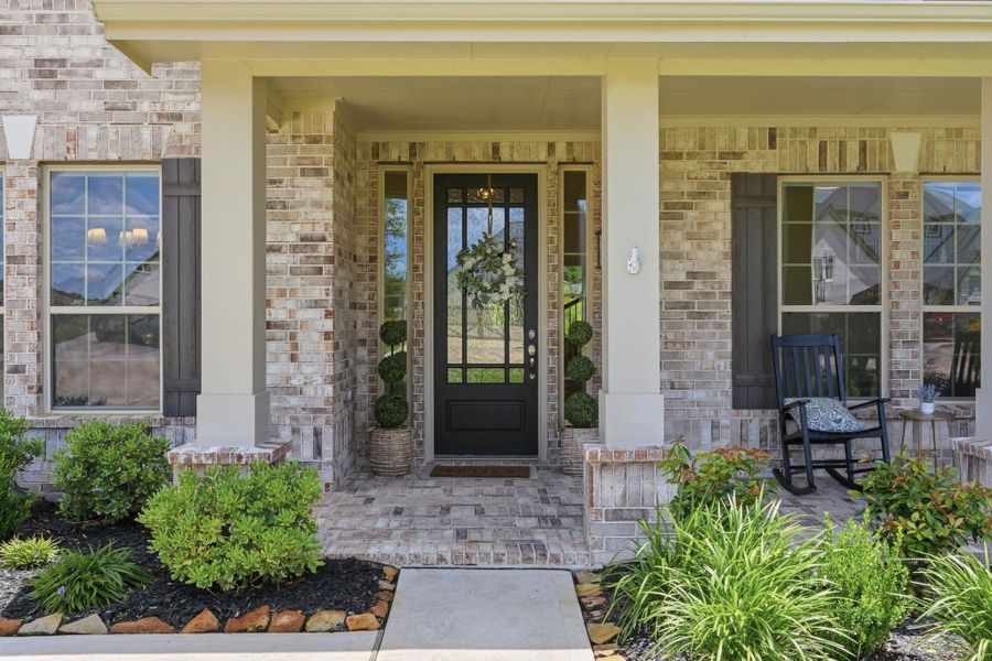 Charming front porch with brick exterior, featuring a welcoming custom door, surrounded by lush landscaping.