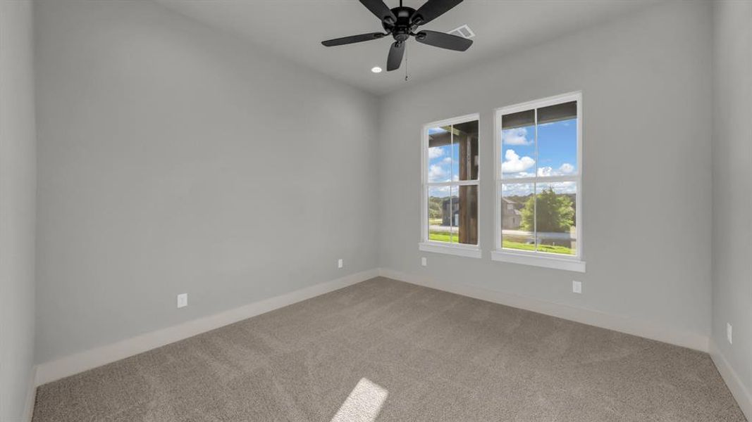 Carpeted interior space featuring light gray walls, white trim, a black ceiling fan with integrated lighting, and two large windows offering expansive outdoor scenery Carpeted interior space featuring light gray walls, white trim, a black ceiling fan with integrated lighting, and two large windows offering expansive outdoor scenery