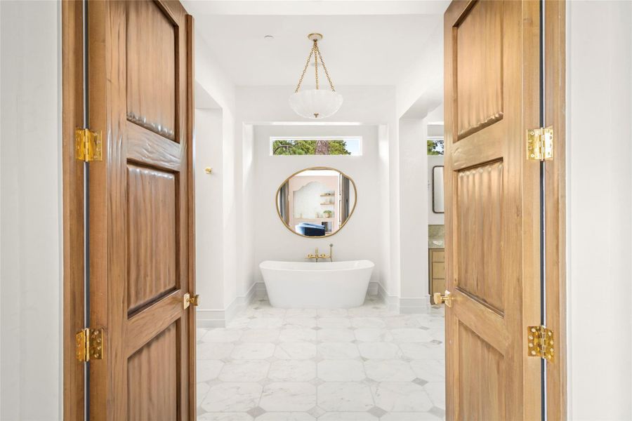 Venetian plaster walls set the tone in the primary bath, where a freestanding soaking tub, softly veined marble flooring, warm brass fixtures, and custom wood doors create a beautifully layered retreat. A sculptural pendant and abundant natural light complete the space. Venetian plaster walls set the tone in the primary bath, where a freestanding soaking tub, softly veined marble flooring, warm brass fixtures, and custom wood doors create a beautifully layered retreat. A sculptural pendant and abundant natural light complete the space.