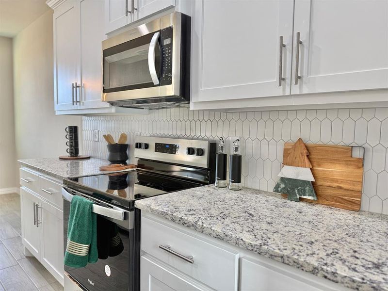 Kitchen with appliances with stainless steel finishes, white cabinets, light stone counters, and decorative backsplash